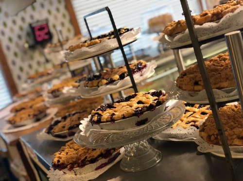 A display of various pies on decorative stands in a bakery, showcasing different flavors and crust designs.