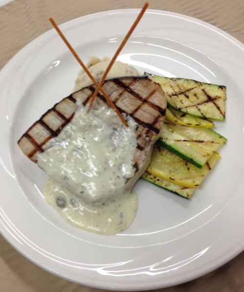 Grilled fish fillet topped with creamy sauce, served with grilled zucchini on a white plate.