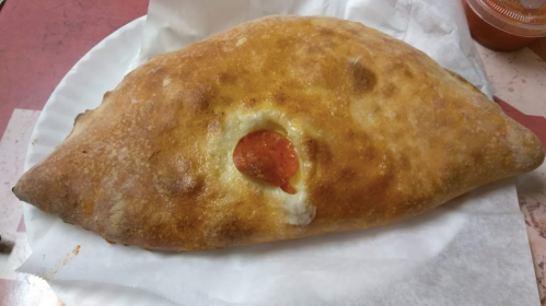 A golden-brown calzone with a visible pepperoni slice and cheese filling, served on a white plate.