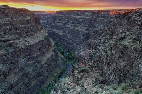 A stunning canyon landscape at sunset, showcasing steep rock formations and a winding river below.