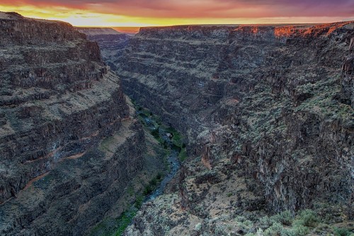 A stunning canyon landscape at sunset, showcasing steep rock formations and a winding river below.