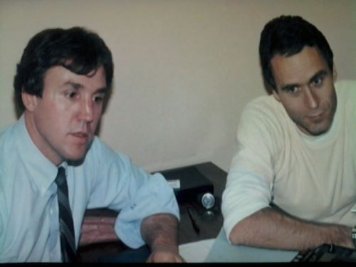 Two men sit at a table, engaged in conversation, with a serious expression on their faces.