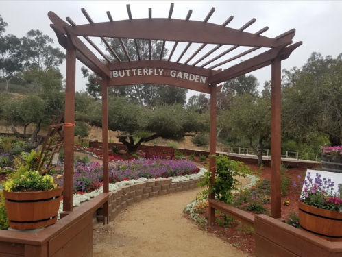 A wooden archway labeled "Butterfly Garden" leads into a colorful garden with flowers and greenery.