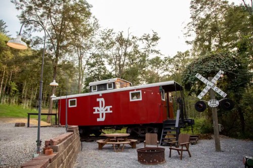 A red train caboose converted into a cozy accommodation, surrounded by trees and a fire pit area.