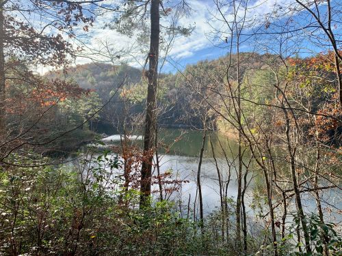 A serene lake surrounded by trees and hills, reflecting the sky and autumn foliage.
