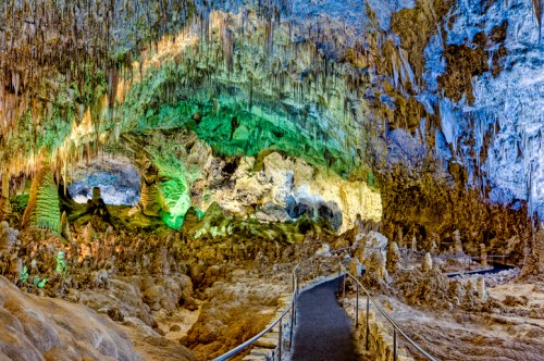 A colorful cave interior with stalactites and stalagmites, featuring a winding pathway illuminated by vibrant lights.