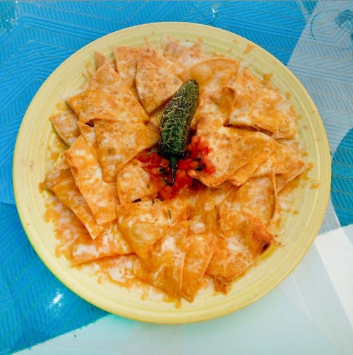 A plate of cheesy nachos topped with diced tomatoes and a green chili, served on a yellow dish.