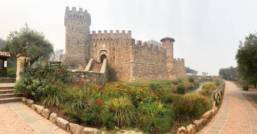 A stone castle with towers surrounded by colorful flowers and greenery, set along a pathway.