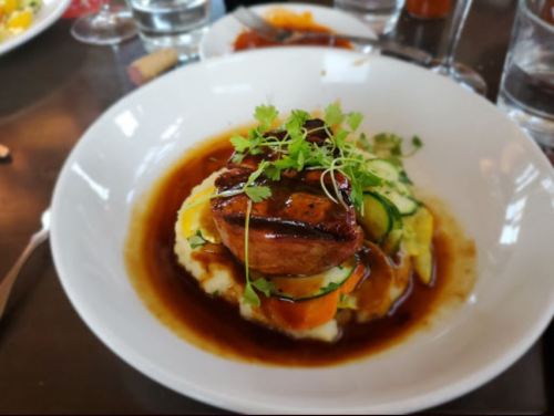 A plate of mashed potatoes topped with glazed meat, garnished with herbs and served with a rich sauce.