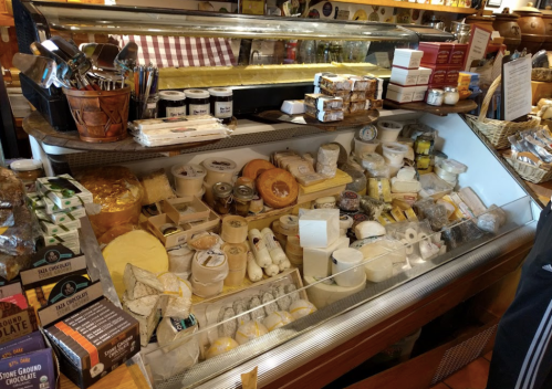 A display case filled with a variety of cheeses, jars, and gourmet food items in a cozy shop setting.