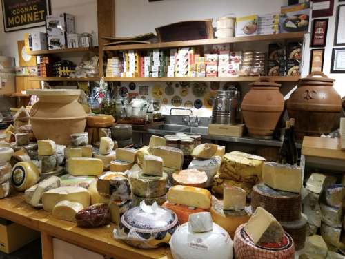 A variety of cheeses displayed on a wooden table, with jars and containers in the background.