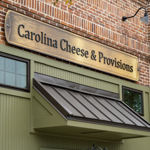 Sign for "Carolina Cheese & Provisions" on a brick building with a green facade and awning.