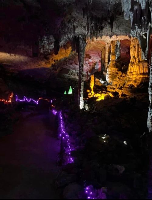 A dimly lit cave with colorful lights illuminating stalactites and stalagmites, creating a mystical atmosphere.