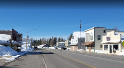 Snow-covered street in a small town, featuring shops and clear blue skies.