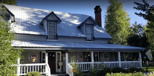 A charming two-story house with a metal roof, surrounded by greenery and featuring a welcoming porch.