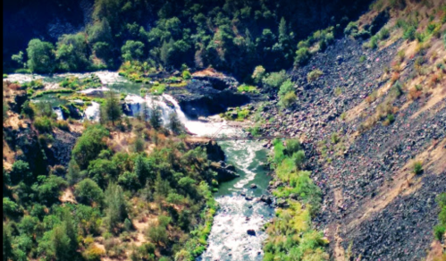Aerial view of a winding river surrounded by rocky terrain and lush greenery.