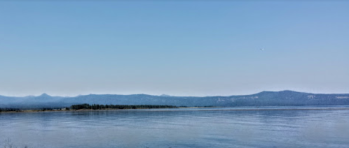 A calm lake reflects a clear blue sky, with distant mountains lining the horizon.
