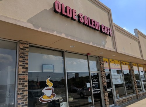 Exterior of Olde Salem Café, featuring a sign and a coffee cup logo, with a clear blue sky in the background.