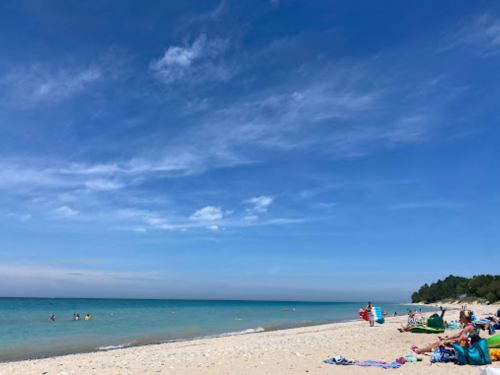 A sunny beach scene with clear blue skies, gentle waves, and people relaxing on the sand.