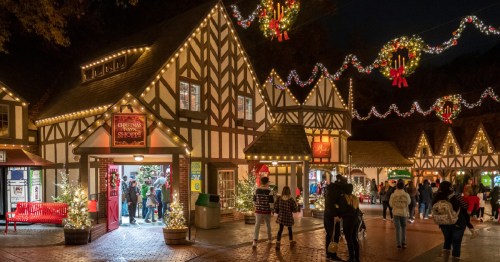 Festively decorated shops with lights and wreaths, bustling with people during a winter evening.