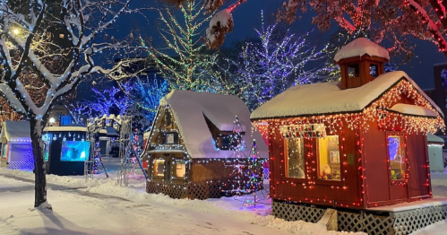 Colorful, illuminated cabins surrounded by snow and festive lights in a winter wonderland at night.