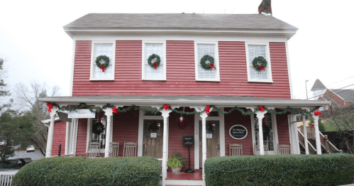 A red house decorated with wreaths and holiday garlands, featuring a porch and white trim.