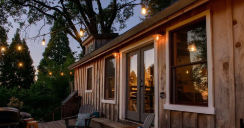 Cozy wooden cabin exterior at dusk, adorned with string lights and surrounded by trees.