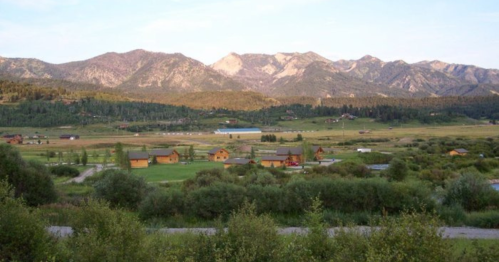 A scenic view of mountains in the background, with a lush green valley and small wooden houses in the foreground.