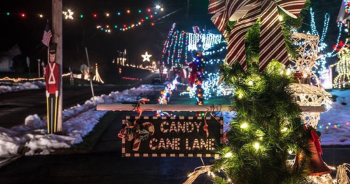 A festive street scene with colorful holiday lights, a sign reading "Candy Cane Lane," and decorations in the snow.