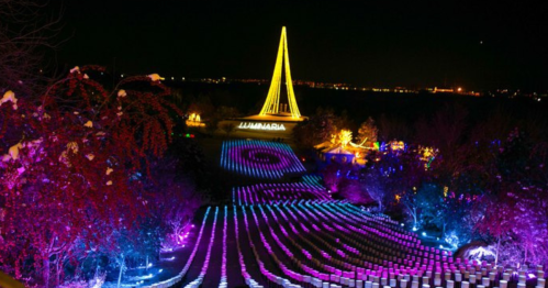 A vibrant light display at night featuring colorful patterns and a tall illuminated structure in the background.