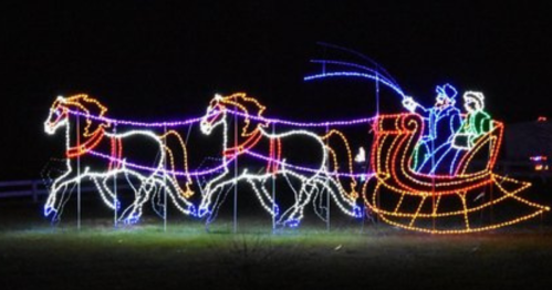 Colorful holiday lights depict a sleigh pulled by two horses, with two figures riding in the sleigh against a dark background.