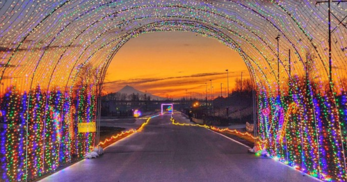 A colorful light tunnel arches over a road at sunset, with a mountain silhouette in the background.