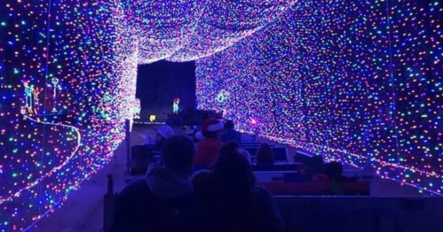 A colorful tunnel of twinkling lights with people sitting in a vehicle, enjoying a festive display.
