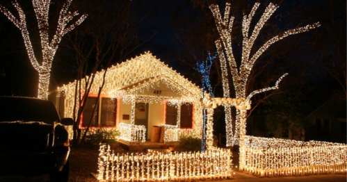 A house decorated with bright white lights, surrounded by illuminated trees and a festive fence at night.
