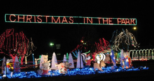 Colorful holiday lights display with "Christmas in the Park" sign and festive animal decorations in a park setting.