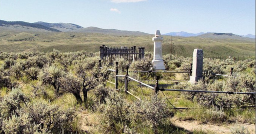 A secluded graveyard surrounded by sagebrush and rolling hills under a clear blue sky.