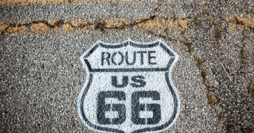 A painted sign on a cracked road marking "Route US 66" in a classic shield shape.
