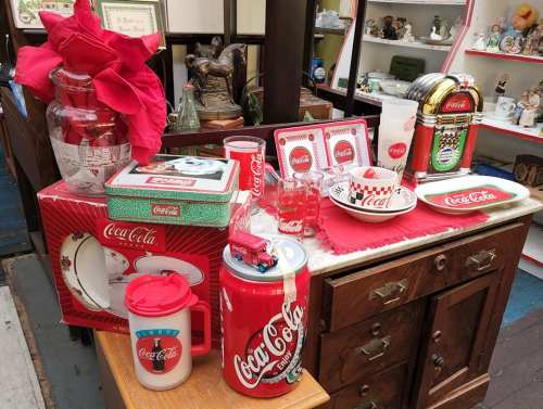A display of vintage Coca-Cola memorabilia, including glasses, plates, and a decorative truck, on a wooden table.