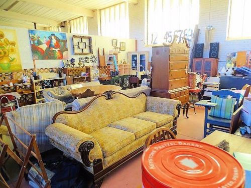 A cluttered antique shop filled with furniture, artwork, and various items, including a vintage sofa and wooden dresser.