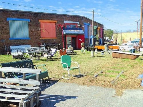 A vintage shop exterior with colorful shutters, outdoor furniture, and a grassy area under a clear blue sky.