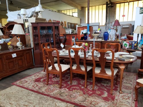 A spacious room filled with vintage furniture, including a wooden dining table set and various decorative items.