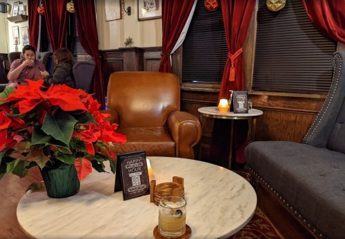 Cozy lounge with a leather chair, a marble table, festive flowers, and warm lighting, creating a welcoming atmosphere.
