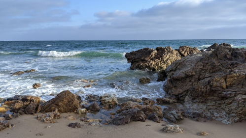 Rocky shoreline with gentle waves lapping against the rocks under a cloudy sky.