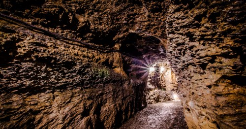 A dimly lit cave tunnel with rugged stone walls and a path illuminated by soft lights.