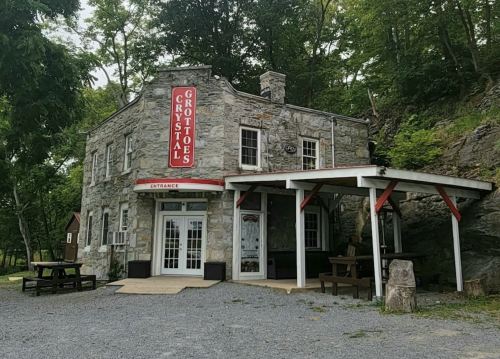 Historic stone building with a red sign reading "Crystal Grottoes," surrounded by trees and gravel pathways.
