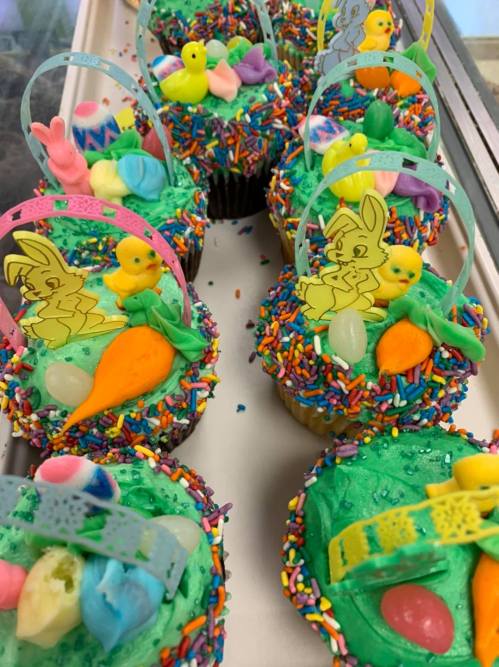 Colorful cupcakes with green frosting, sprinkles, and festive decorations like bunnies, chicks, and candy.