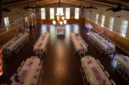 A spacious event hall set up for a gathering, featuring long tables decorated with purple accents and string lights.