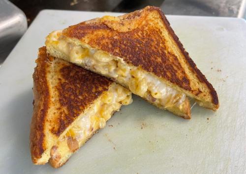 A grilled cheese sandwich with melted cheese and macaroni filling, cut into two triangles on a cutting board.