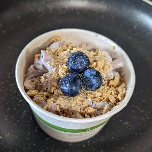 A cup of dessert topped with crushed graham crackers and three blueberries.