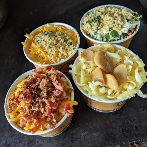 Four cups of pasta with various toppings: breadcrumbs, herbs, bacon, and cheese.